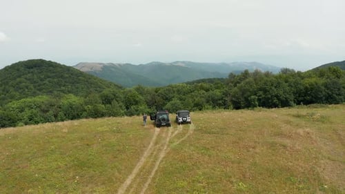 Off road drive in Georgian mountains. Aerial view of parked SUV's and people. Green lush hills in th