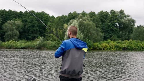 Fisherman with fishing rod or spinning rod and professional tools standing on the river bank