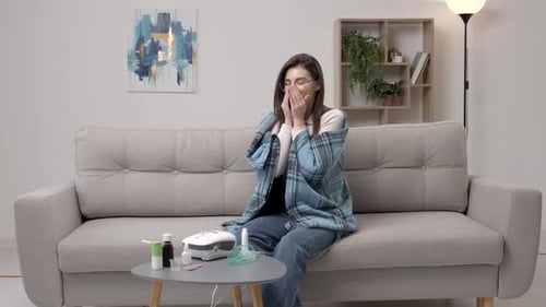 Jeune femme portant des vêtements décontractés, utilisant un spray nasal pour faciliter la respiration, assise sur un canapé