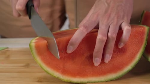 Hands of young woman european cuts watermelon into slices with kitchen knife on cutting board