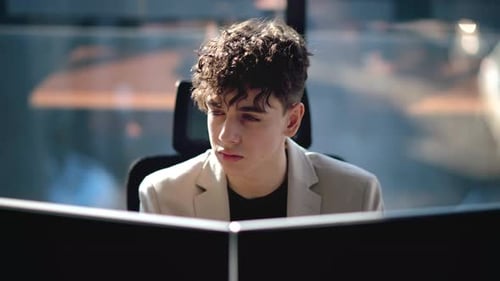 Young man is working in a computer in an office, windows on the background