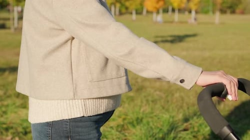 Young Mother Gently Rocks Stroller Walking in Park with Baby
