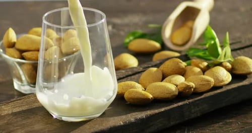 The almond milk is poured into a glass in slow motion, the background in woods there are almonds,