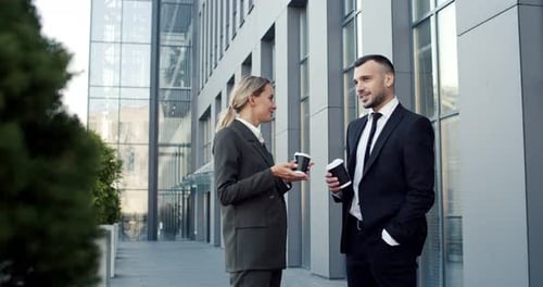 Kaukasisches, fröhliches junges Geschäftspartnerpaar, das zusammen durch die Stadt geht, sich unterhält und