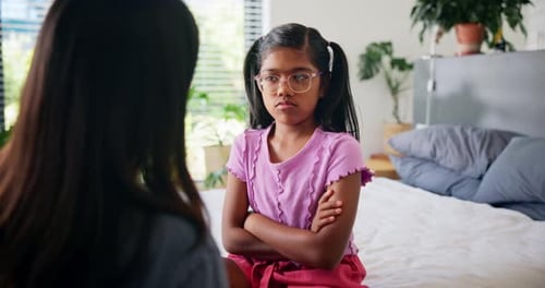 Unhappy Girl with Crossed Arms Sits on Bed