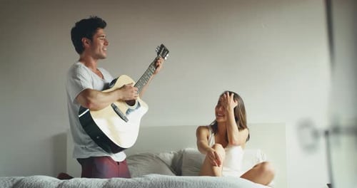 Young Man Plays Guitar for Girlfriend in Bedroom