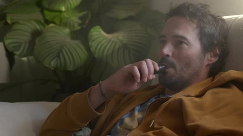 Relaxed Caucasian young man smoking an electronic cigarette device on Couch, Close-up shot