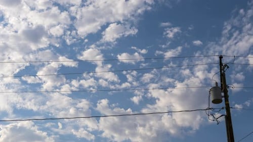 Fluffy clouds float by over the power lines - time lapse cloudscape