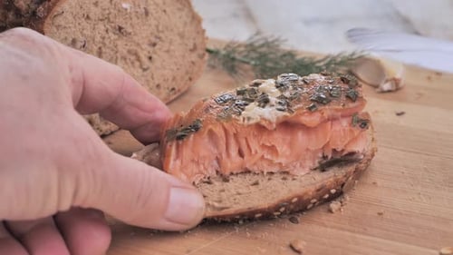 Ein Mann legt geräucherten Lachs auf ein Stück Brot und fügt einen Dillzweig auf ein Holzschneidebrett