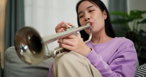 Young Woman Plays Trumpet on Couch Indoors