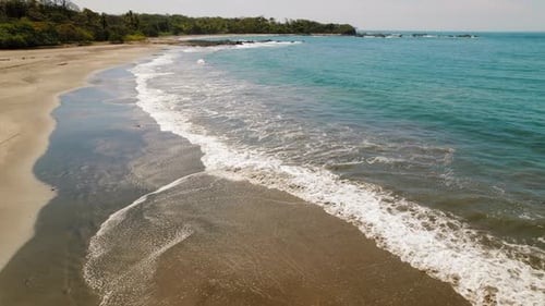 Serene tropical beach with gentle turquoise waves and dark sand in Costa Rica