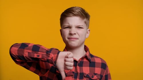 Boy Showing Thumbs Down at Camera on Yellow Background
