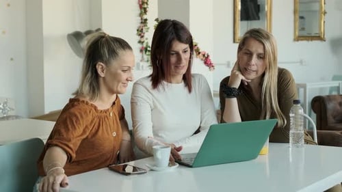 Three Women Using a Laptop Together While Sitting in a Coffee Shop