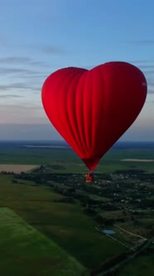 Red airship in the shape of a heart. Hot air balloon in the sky over a field