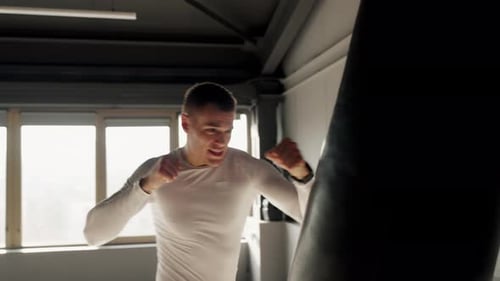 Focused Young Man Performing Shadow Boxing in Sunny Gym