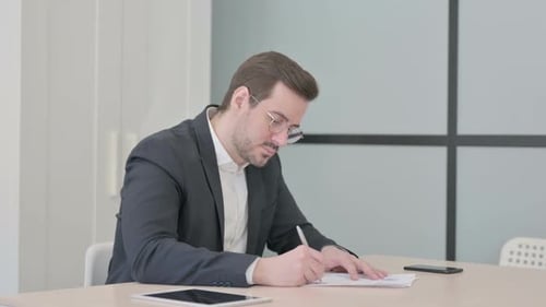 Man Reviews Documents at Desk in Office