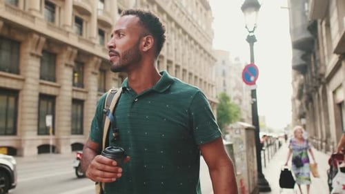 Young man walks down the street looking around with hot drink in his hands