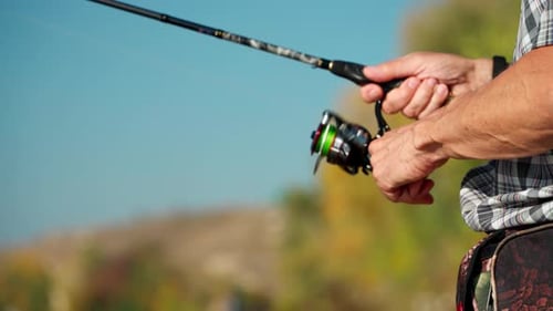 Hands of a mature male fisherman close-up spinning a reel on a spinning rod