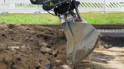 Excavator working on road construction site. Excavator bucket collects dirt with stones in dirt pile