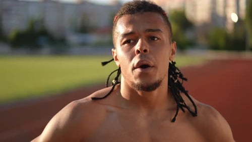 Slow Motion Closeup After a Long Run Along the Stadium Running Track a Male Athlete with Dreadlocks