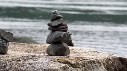 Slow tracking shot of two small cairns stacked on a boulder by the sea.