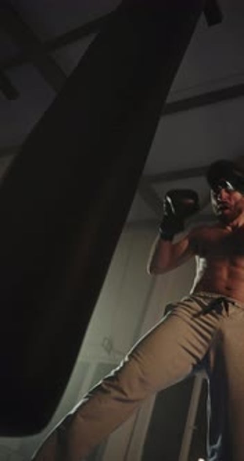 Shirtless Man Boxing Punching Bag in Dark Gym