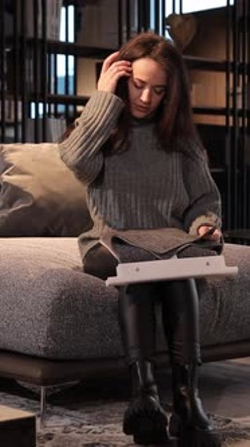 Beautiful Longhaired Woman Sitting on a Sofa in a Furniture Showroom and Looking at a Catalog