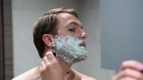 Man Shaving Beard in Bright Bathroom at Home