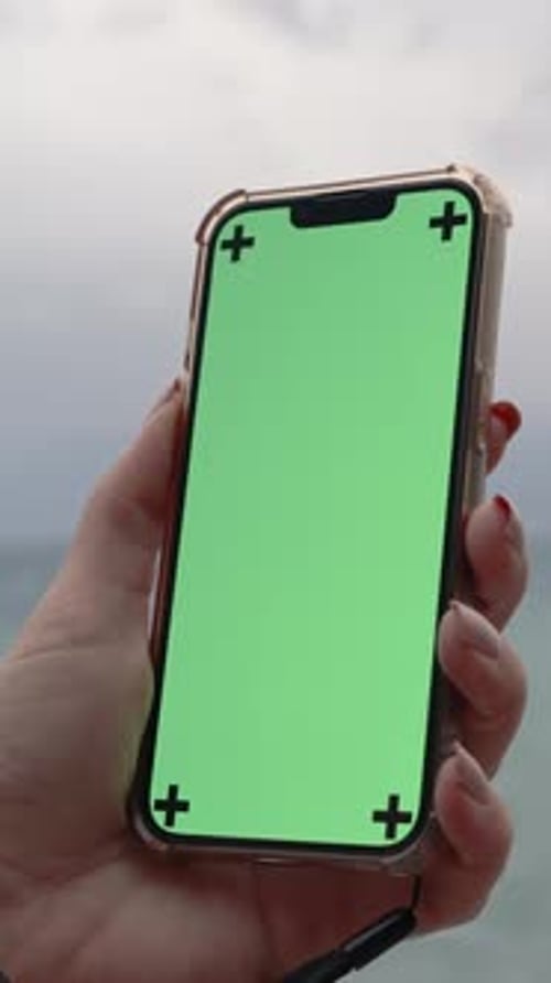 Vertical video. A Female Hand Holds a Mobile Phone with a Mockup of an Empty Green Screen.
