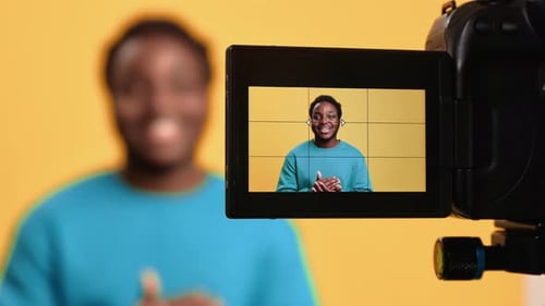 Lächelnder Afro-Mann-Influencer dreht Videoblog, Vlog-Kamerabildschirm, posiert isoliert im Orange Studio