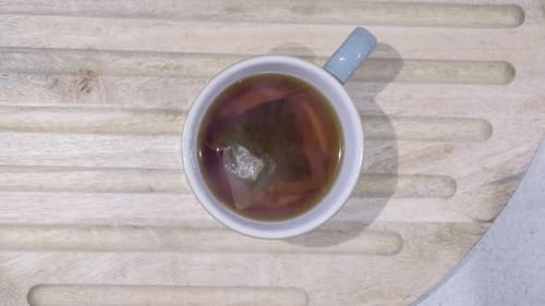 Ansicht von oben auf eine blaue Tasse mit Tee und Teebeutel, wobei Dampf in Richtung Kamera aufsteigt. Fokusverschiebungen f