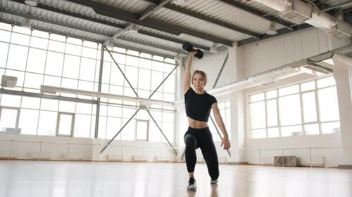 Young Blondehaired Woman Lifting Dumbbell in Beautiful Gym Studio