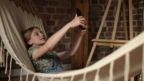 Child Relaxes in Hammock Using Smartphone Indoors