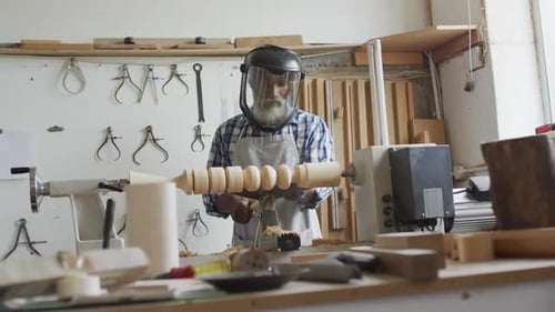 African american male carpenter wearing protective helmet turning wood on a lathe at carpentry shop