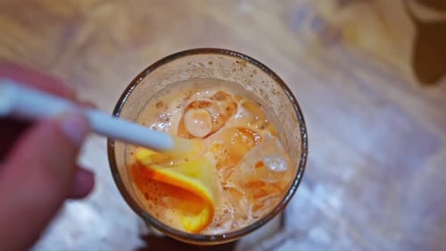 Closeup Top View a Hand Holds a Straw a Man Stirs a Cocktail with Orange