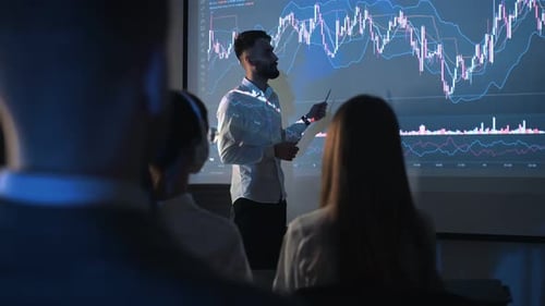 Man Presents Graph to Audience in Dim Workplace