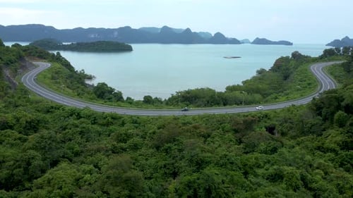 Scenic winding road with cars driving through lush tropical jungle overlooking the sea in Langkawi