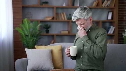 Ill Man Holding Cup and Tissue on Couch