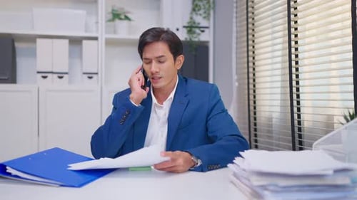 Asian busy businessman talk on phone and look at paper working in office.