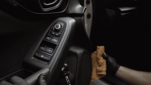 Close up of a male wearing black gloves cleaning a white car with black interior with a microfiber c