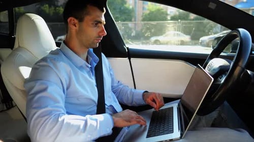 Handsome Entrepreneur Working on Notebook While Riding an Autonomous Self Driving Electric Car at