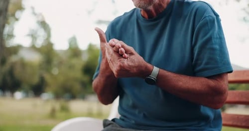 Mature Man Rubbing Hands On Park Bench