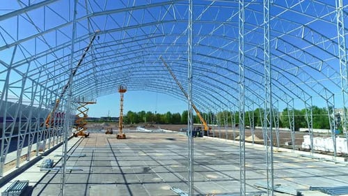 Plataforma rodante aérea que atraviesa una gran estructura con andamios y grúas de construcción