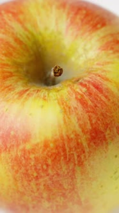 Rotating apple closeup with glossy red and yellow gradient and detailed stem, vertical view