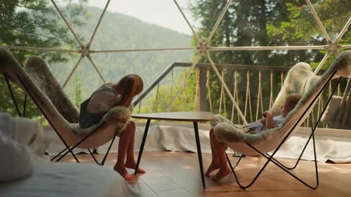 Siblings Sit in Woolen Chairs in Glamping Overlooking Forest