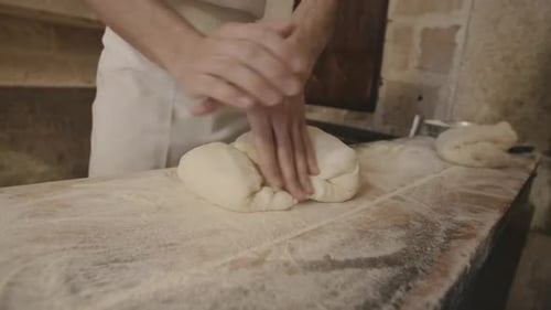 A baker is quickly folding and kneading some dough in a bakery.