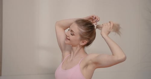 Woman Puts Hair in Ponytail Indoors Smiling
