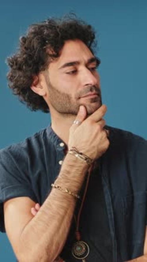 Pensive man rubbing his chin and looking side isolated on blue background in studio