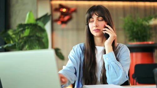 Young Woman on Phone Working at Laptop