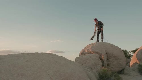 Un joven músico punk se para sobre una gran roca, aplasta su guitarra con frustración y luego la tira